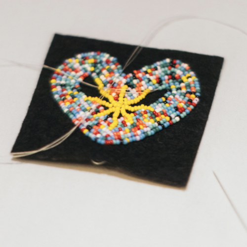 Beaded heart pendant stitched with colorful seed beads on a black fabric square, with thread trailing from the edges